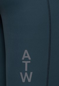 Granatowe legginsy sportowe wykonane z elastycznego materiału, z płaskimi szwami i szarym logo 'ATW' po boku. Gładka tekstura.