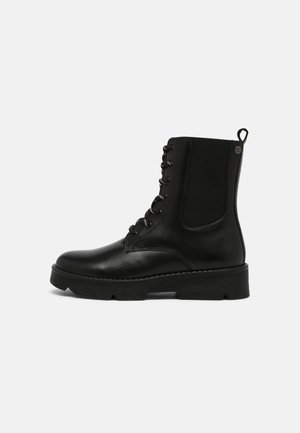 Botte de combat en cuir noir avec laçage à l'avant, panneau latéral élastique, languette de traction au talon et semelle épaisse à rainures, vue de côté.