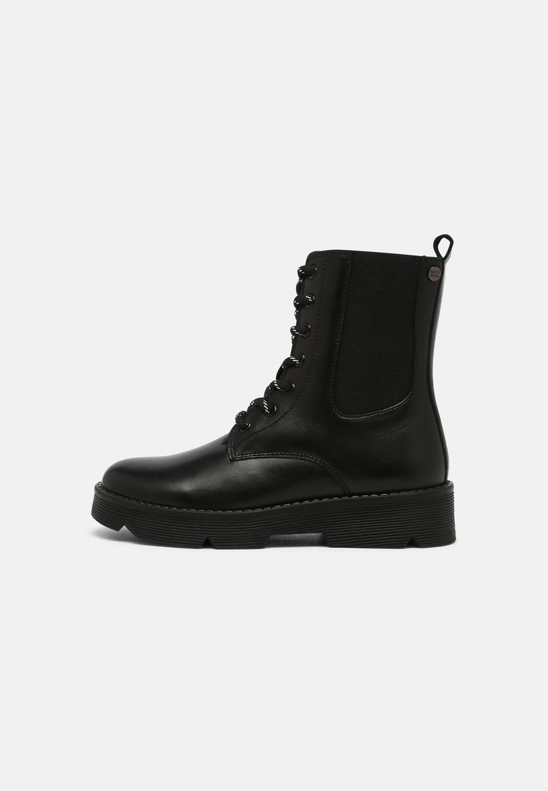 Botte de combat en cuir noir avec laçage à l'avant, panneau latéral élastique, languette de traction au talon et semelle épaisse à rainures, vue de côté.