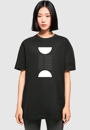 Svart oversized t-skjorte laget av bomull, med et sentralt hvitt grafisk design bestående av to halvsirkler og horisontale linjer.