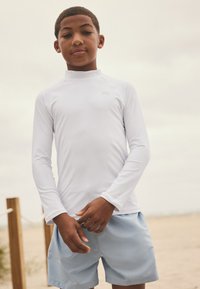 Vit långärmad rashguard kombinerad med ljusblå badshorts. Mjukt tyg med figurnära design och minimal logotyp.