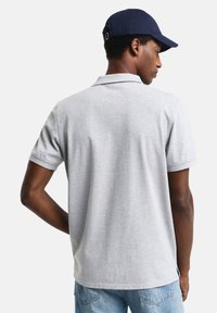 Grå polo skjorte med korte ærmer, med krage og ryggventil. Marineblå caps med rem, denimjeans fullfører det uformelle utseendet.