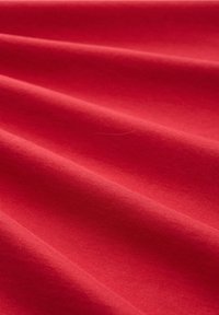 Roter Baumwollstoff mit einer glatten Textur und dezenten Glanz, der sanfte Wellen und Falten aufweist und Tiefe sowie Dimension erzeugt.