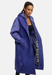 Long blue coat with a hood, featuring a mix of fabric textures, an open front design, and a bright yellow logo inside.