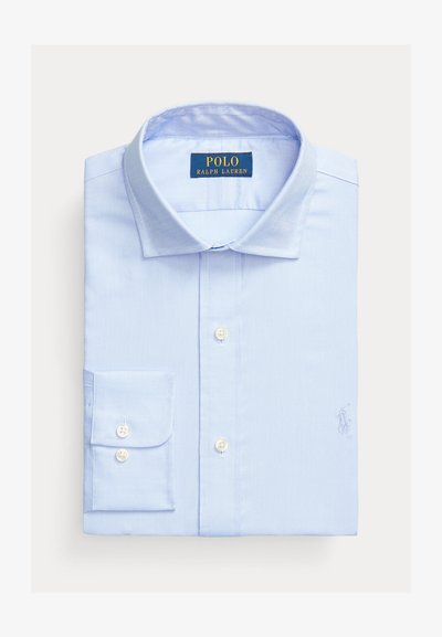 Camisa azul clara com botões, com um pequeno logótipo bordado no peito, um colarinho clássico e mangas longas com punhos abotoados.