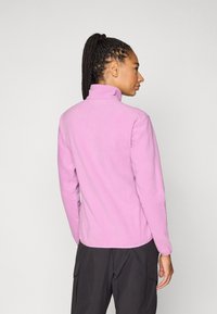 Fleecejakke i pastellrosa, med høy krage og lange ermer, vist bakfra. Glatt tekstur med en romslig passform.