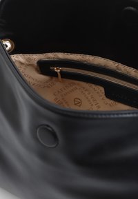 Indvendigheden af den sorte lædertaske har en glat tekstur, med en lynlås lomme og en beige foret, der har et gentaget "Café Noir" tekstmønster.