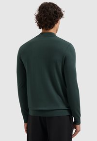 Donkergroene langemouwen trui van zacht materiaal, met een ronde kraag en geribbelde manchetten, met een gladde textuur en minimale details.