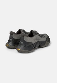 Scarpe da ginnastica grigie con tomaia testurizzata, colletto imbottito e suole spesse in Vibram. Tra le caratteristiche ci sono i lacci e il supporto rinforzato per il tallone.