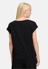 Svart t-shirt med kort ärm, avslappnad passform, rund halsringning och mjukt bomullstyg. Sömmar vid axlarna och nederkanten.