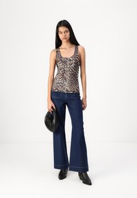 Top s uzorkom leopard, s izrezom oko vrata, u kombinaciji s širokim tamnim trapericama i crnim čizmama s potpeticom, nosi crnu torbu.