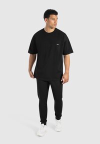 Schwarzes T-Shirt mit kurzen Ärmeln und schwarze Jogginghosen aus Baumwolle. Das Outfit hat ein kleines Logodetail und wird mit weißen Sneakers kombiniert.