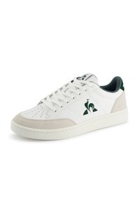 Białe niskie sneakersy z beżowymi zamszowymi akcentami, białymi sznurówkami, perforowanym noskiem oraz ciemnozielonym logo koguta po boku i na zakładce pięty.