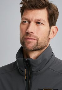 Gray zip-up jacket with a high collar, featuring black accents and a PME Legend label. Smooth material with a structured fit.