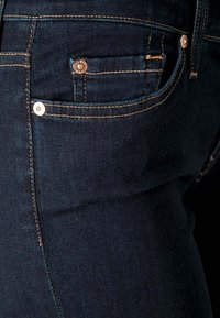 Vaqueros de mezclilla azul oscuro que cuentan con un bolsillo frontal con costura visible, botón de metal y una ligera textura. Diseño ajustado con detalles sutiles.