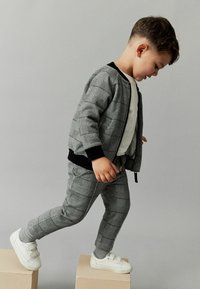 Grå rutig träningsdräkt i mjukt material, bestående av en bomberjacka med svart kant och matchande tapered byxor, kombinerat med vita sneakers.
