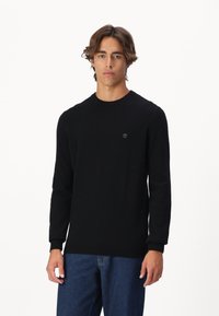 Schwarzer Pullover mit langen Ärmeln in einem einfarbigen Strickdesign, mit Rundhalsausschnitt, gerippten Bündchen und kleinem Logo auf der Brust.
