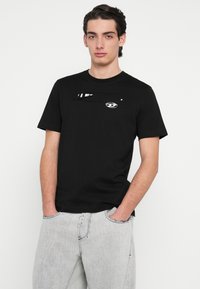 Fekete pamut rövid ujjú póló. Mellrészén grafikus mintával, normál szabással és kerek nyakkivágással.