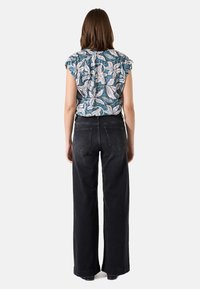 Bloemmotief top in teal, met korte gerimpelde mouwen, gecombineerd met hoge zwarte wijde jeans en donkere, gehakte enkellaarzen.