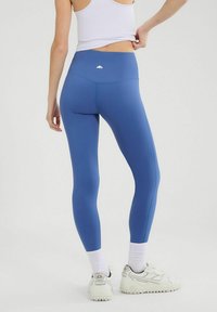 Granatowe legginsy z wysokim stanem wykonane z elastycznego materiału. Gładka faktura w jednolitym kolorze z kontrastowym szwem. Białe logo z tyłu.
