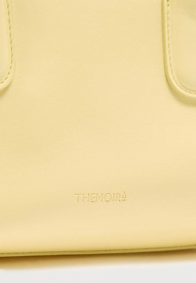 Ανοιχτό κίτρινο δερμάτινο τσάντα χειρός με ανάγλυφο το όνομα της μάρκας "THEMOIRè" κοντά στο κάτω κέντρο και διπλές λουράκια στο πάνω μέρος.