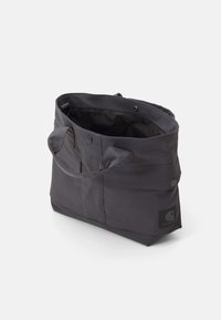 Tummanharmaa kangaskassi, jossa on kaksi kantokahvaa, napitus ja etutaskut. Varustettu mustalla logotarralla. Teksturoitu pinta ja kestävä muotoilu.