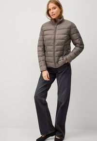 Grijze gewatteerde pufferjack met een hoge kraag en een rits aan de voorkant. Gecombineerd met donkere denim wijde broek en zwarte instapschoenen.
