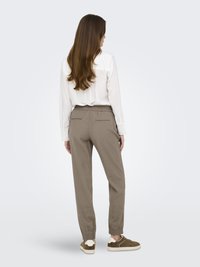 Chemisier léger blanc avec empiècement dans le dos, associé à un pantalon khaki fuselé avec une taille élastique et des ourlets pliés, porté avec des baskets marron.