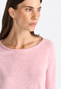 Lichtroze langemmouwen top met een ruime halslijn met ruwe randen. Zachte stof met een licht gestructureerde afwerking, ideaal voor casual gebruik.