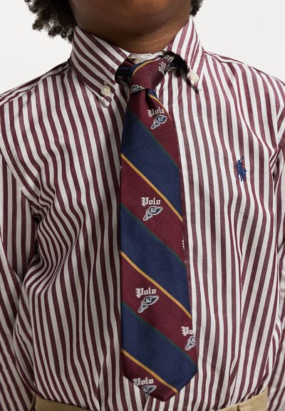 Bordo un balti svītrains krekls ar pogām, ko papildina zils kaklasaite ar diagonālām svītrām un logotipa akcentiem.