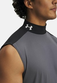 Szary bezrękawnik sportowy z wysokim czarnym kołnierzem, z logo Under Armour w kolorze srebrnym na kołnierzu. Gładki, elastyczny materiał, dopasowany krój.