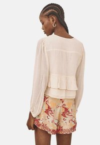 Top peplum de crema con mangas largas, combinado con pantalones cortos estampados que presentan remolinos en colores pastel y un ribete rojo. Detalle de tejido texturizado visible.