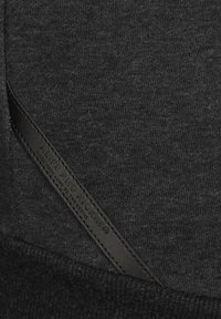 Sudadera negra con tejido texturizado, que presenta una etiqueta de cuero grabada con "ALIFE AND KICKIN". La etiqueta está situada cerca del bolsillo.