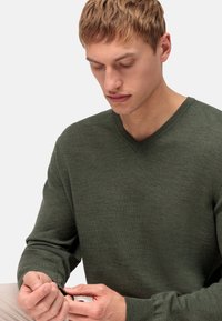 Groene v-hals trui van zacht materiaal, met lange mouwen en geribbelde manchetten, met een gladde textuur en subtiele variaties in kleur.