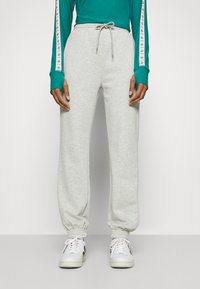 Calças de moletom cinzentas com cintura ajustável e punhos elásticos, combinadas com uma blusa de manga longa turquesa com riscas contrastantes nas mangas.