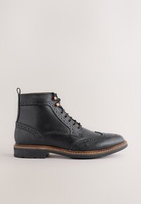 Schwarzer Leder-Stiefelette mit Brogue-Details, runder Schuhspitze, Schnürung vorne und brauner Naht entlang der hellbraunen Sohle. Mit einer Zuglasche hinten ausgestattet.
