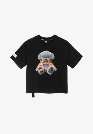 Camiseta negra de manga corta con un oso de peluche gris con una sudadera con capucha naranja impresa en la parte delantera y una pequeña etiqueta blanca en la manga izquierda.
