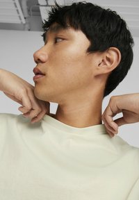 Lys beige bomulds t-shirt med en afslappet pasform, med en rund halsudskæring. Motivet har kort, mørkt hår og kigger til siden.