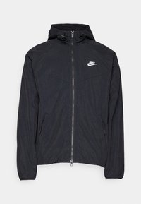 Veste coupe-vent noire à capuche Nike avec fermeture éclair intégrale à l'avant, poches latérales zippées, poignets élastiques et logo blanc sur la poitrine gauche.