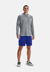 Leichtes graues Langarm-Hoodie-Shirt, kombiniert mit königsblauen Sportshorts, mit einer weichen Textur und Under Armour-Logo.