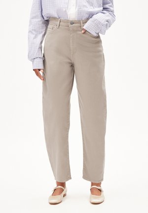 Vrouw draagt beige high-waist taps toelopende broek, licht geruit overhemd met opgerolde mouwen en crèmekleurige Mary Jane flats.