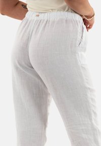 Pantaloni bianchi in lino con vita elastica, tasche laterali e una finitura leggermente strutturata, che mostrano una vestibilità rilassata e un materiale leggero.