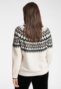 Sweter dziany w kolorze kremowym z geometrycznym czarno-beżowym wzorem na karczku. Posiada ściągacze przy mankietach i u dołu, miękką teksturę i luźny fason.