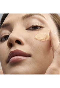 Klar gel applicerad på kinden, som framhäver en jämn hudstruktur. Produkten har en ljusbrun färg, vilket visar på en fuktgivande eller kosmetisk formulering.