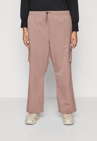 Pantalons cargo légers de couleur rose clair, avec une taille élastique, une fermeture à cordon et des poches latérales. Portés avec des chaussures beiges perforées.
