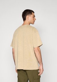 Beige színű, pamut póló, laza fazonnal, kerek nyakkivágással és rövid ujjakkal. Simaság jellemzi, finom, márványozott mintával.