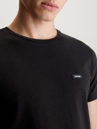 Melnas kokvilnas T-kreklis ar apaļu kaklu un mazu taisnstūra Calvin Klein logo uz kreisā krūtis. Mīksta tekstūra un pieguļoša forma.
