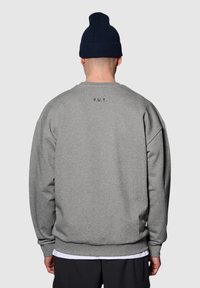 Grijze sweatshirt met een ontspannen pasvorm, geribbelde boorden en zoom. Heeft een bedrukte "F.U.T." op de achterkant, gecombineerd met een marineblauw gebreid beanie.