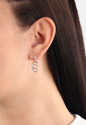 Orecchio di una donna con capelli corti che indossa orecchini a cerchio intrecciati in argento e oro rosa con finiture testurizzate e lisce.
