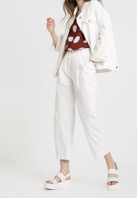 Giacca di jeans bianca, top borgogna con pois bianchi, pantaloni bianchi a vita alta e sandali con piattaforma bianchi con cinturini alla caviglia.